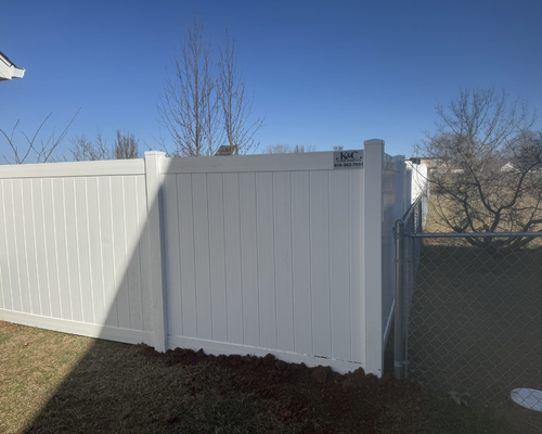 K&C Fence white vinyl PVC privacy fence panel enclosing a backyard along a chain-link fence in Lebanon, Tennessee.