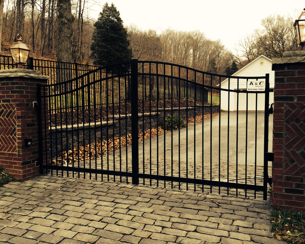 Custom black aluminum driveway gate with self-closing hinges installed between brick columns by K&C Fence in Murfreesboro, TN, providing secure and elegant property access.