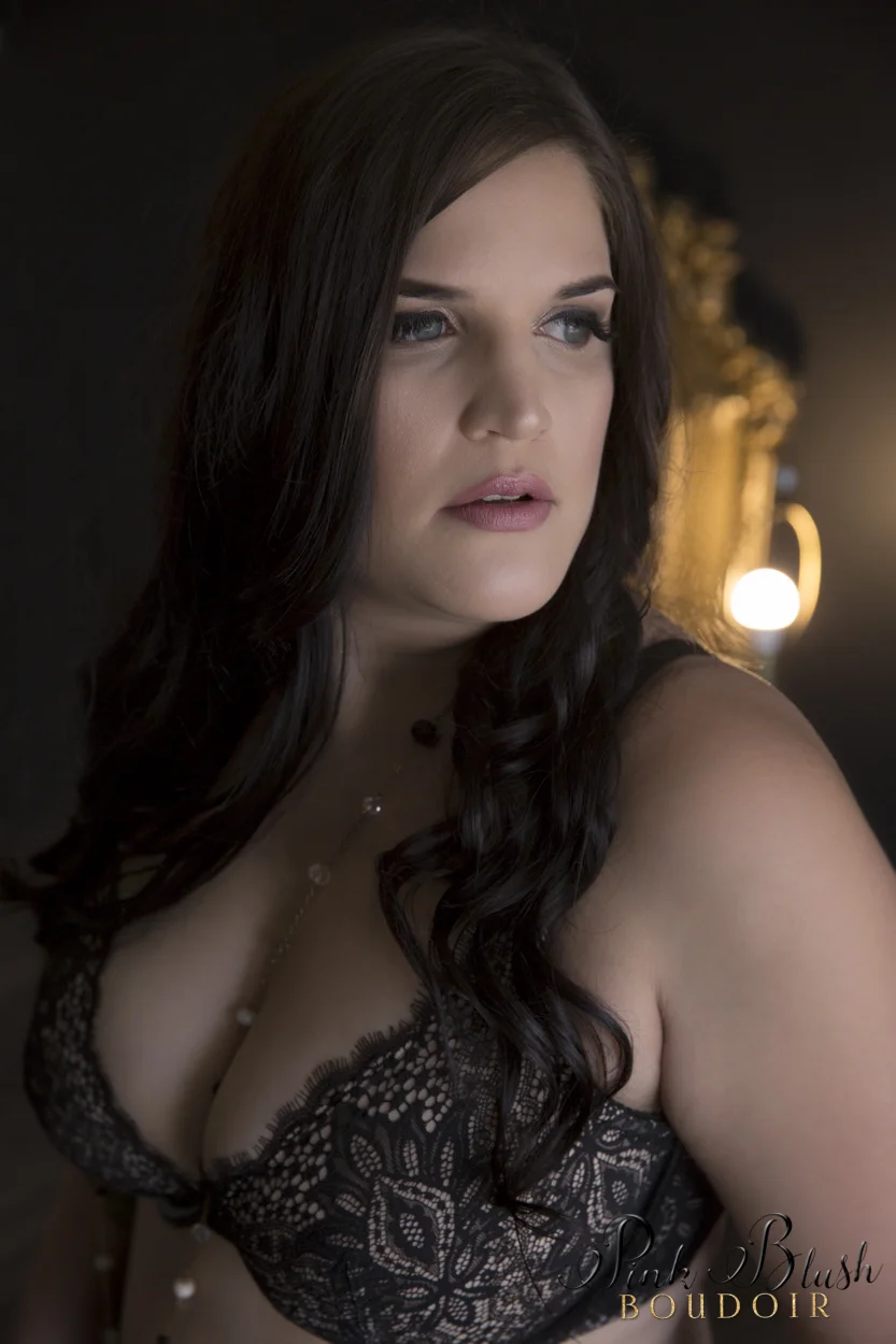 boudoir photography, a curvy woman standing against a black wall