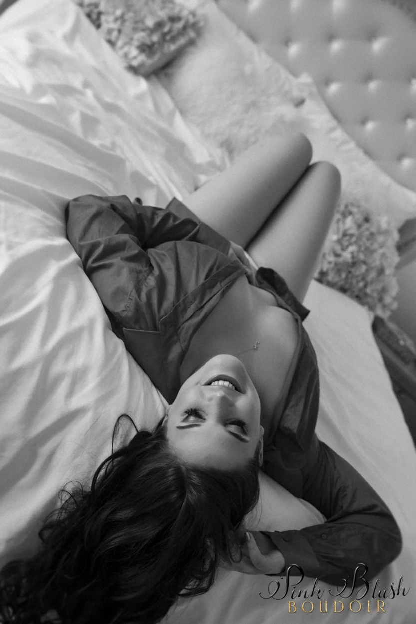 boudoir photography, a woman in a pink button up shirt laying on a bed