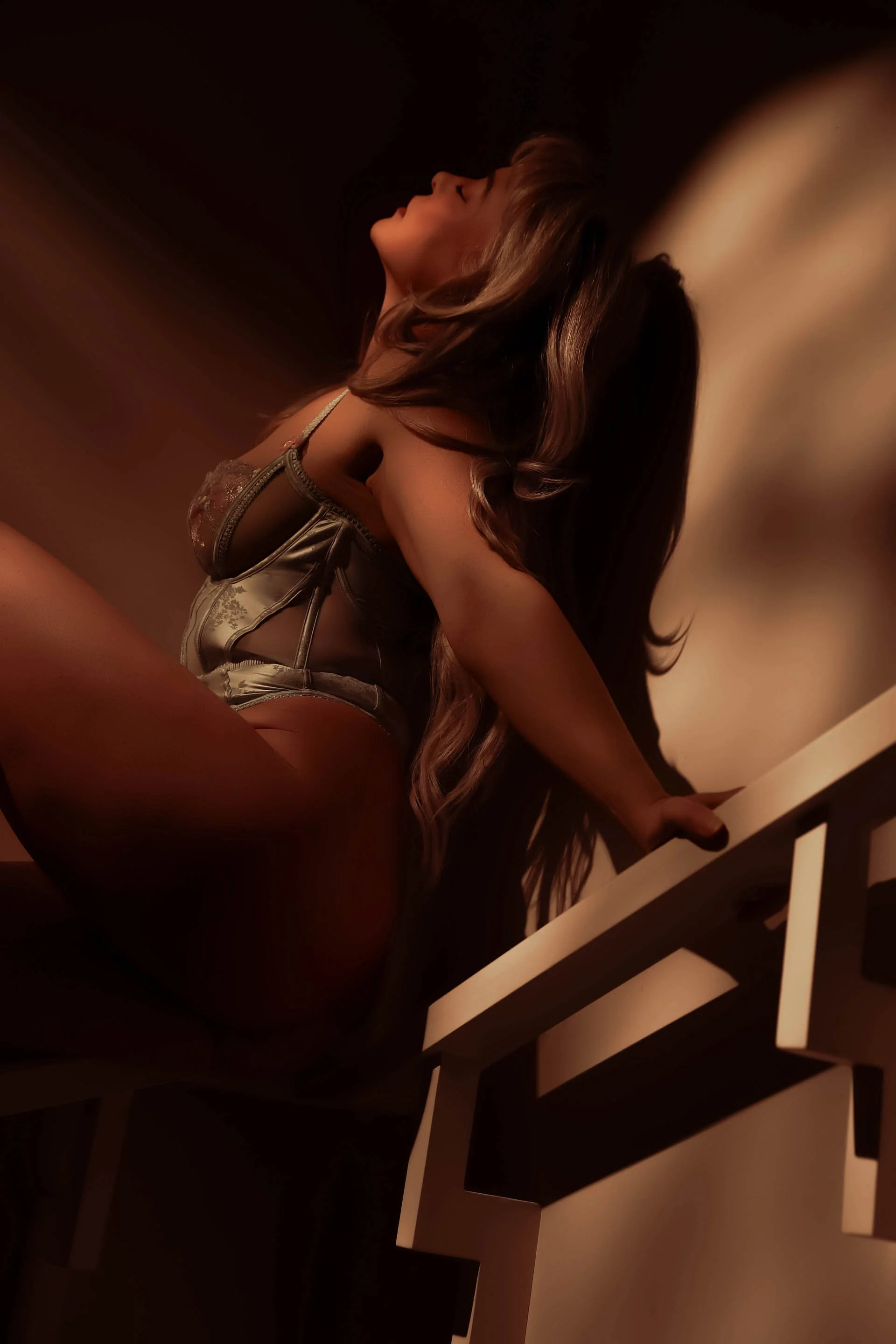 Woman embracing her body in stairwell boudoir photography with warm shadows Edmonton photography studio