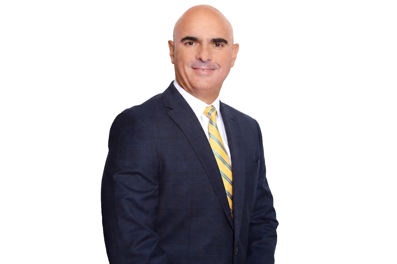 A man in a dark blue suit with a checked pattern, wearing a white shirt and yellow striped tie, smiling and posing against a plain background.