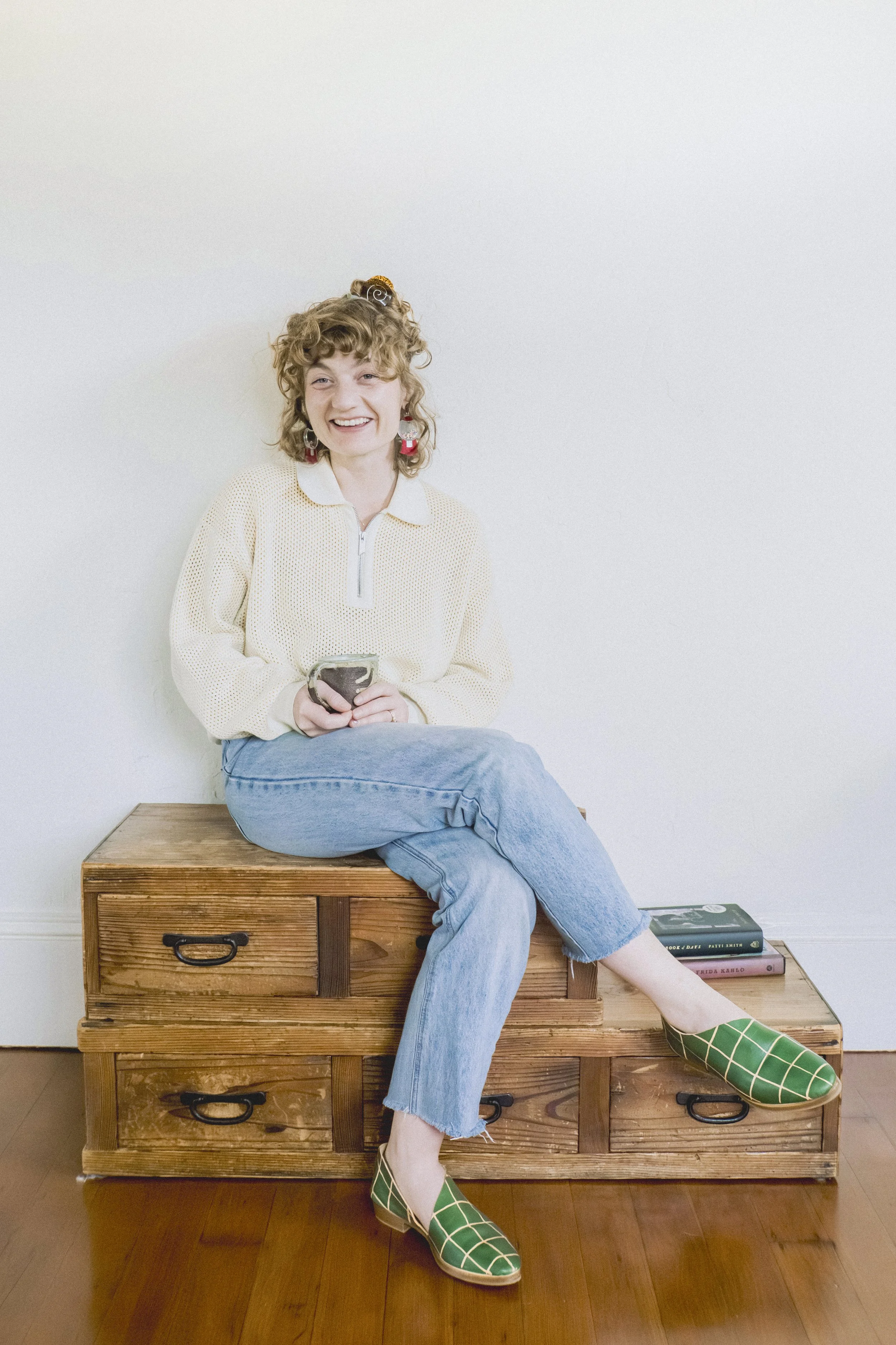 Therapist Mackenzie Studebaker sits crossed legged holding a cup of tea smiling at the camera.