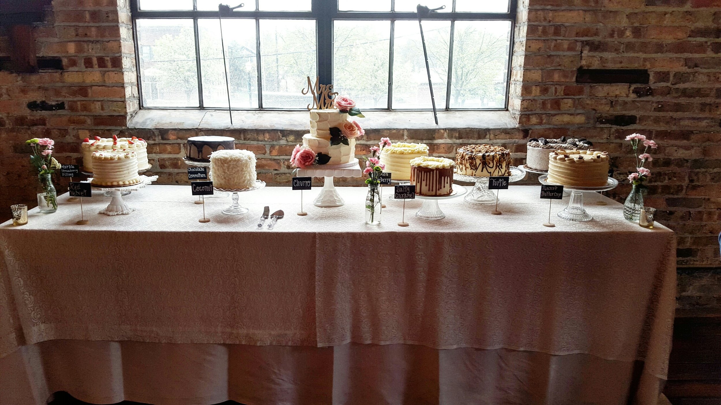 This Sweets Table includes a small tiered cake for the bridal couple's cutting cake, and layered cakes in the following flavors: Red Velvet, Vanilla Strawberry, Chocolate Commotion, Coconut, Lemon Drop, Salty Caramel, Turtle, Oreo and Peanut Butter Cup