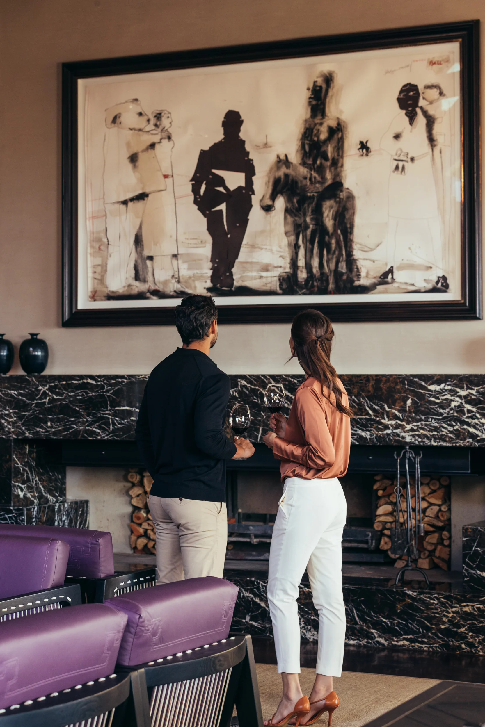 A couple stand by the fireplace and admire an artwork from Laurence Graff’s private collection at the Wine Lounge at Delaire Graff Estate