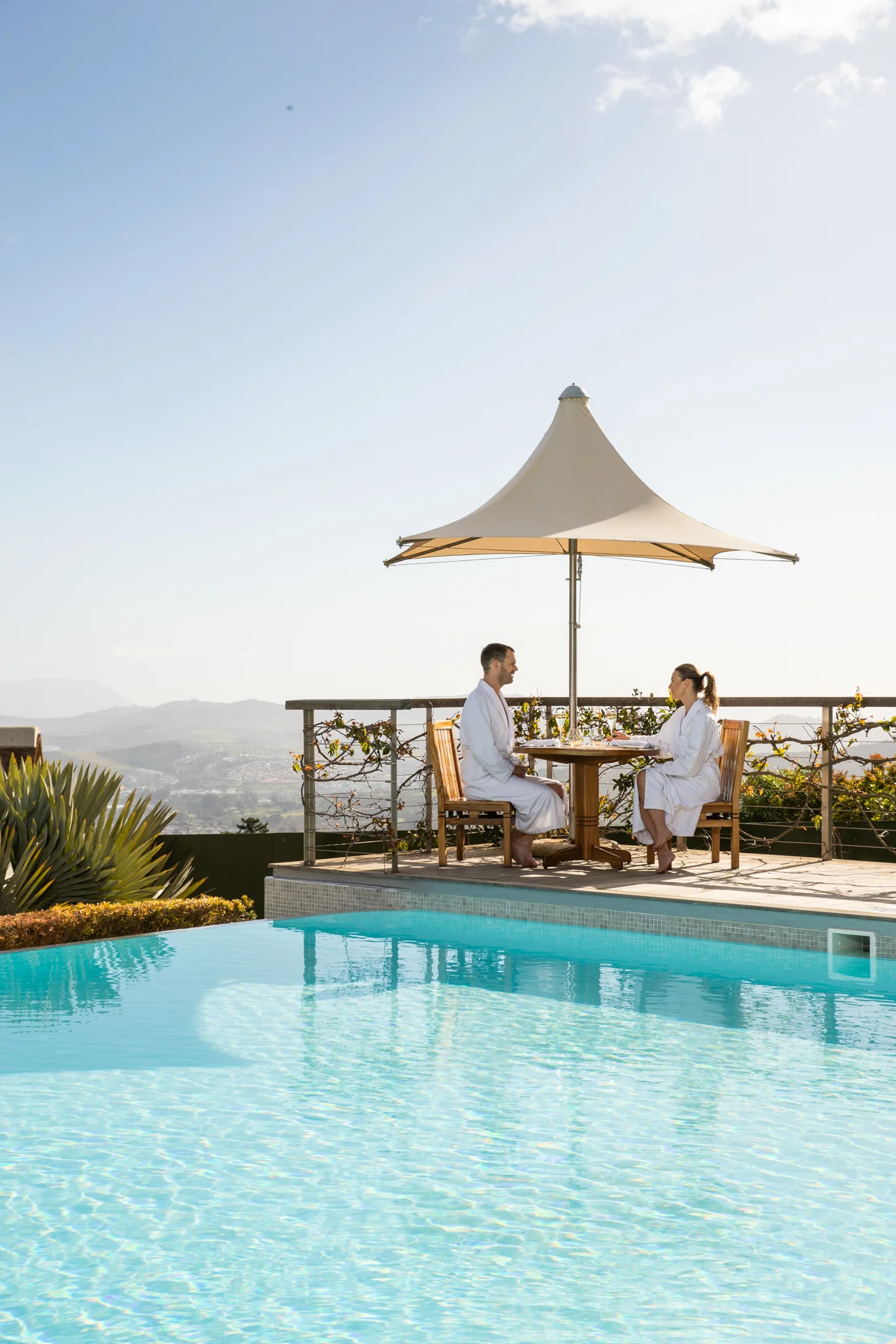 Couple having light lunch on the Delaire Graff Spa deck next to the infinity pool with beautiful views of the Stellenbosch Valley