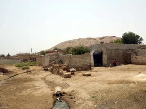 We enter the village. The mound rises behind the houses.