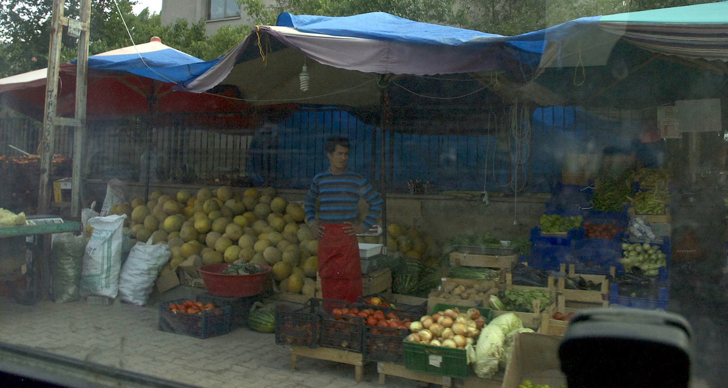 View to a fruit stand through the smudged glass of our vehicle.