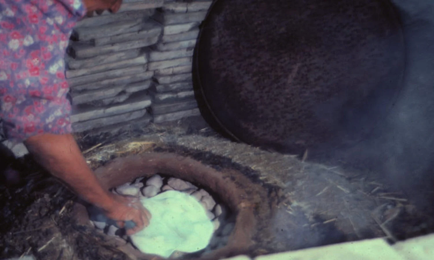A dung-fired bread oven near Madaba, Jordan. The flatbread is cooked on smooth, clean stones. Outside the oven is smoldering dung. The circular metal lid in the back will cover the access hole once the flatbread is flipped.