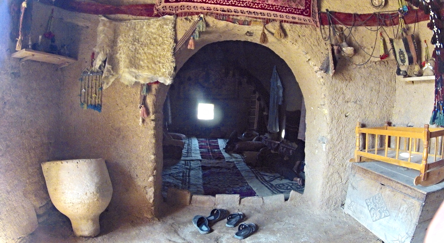A passage between rooms. Men are sleeping on the floor just beyond. The walls are thick, creamy, and colorfully decorated. It is surprisingly clean inside this house of earth!