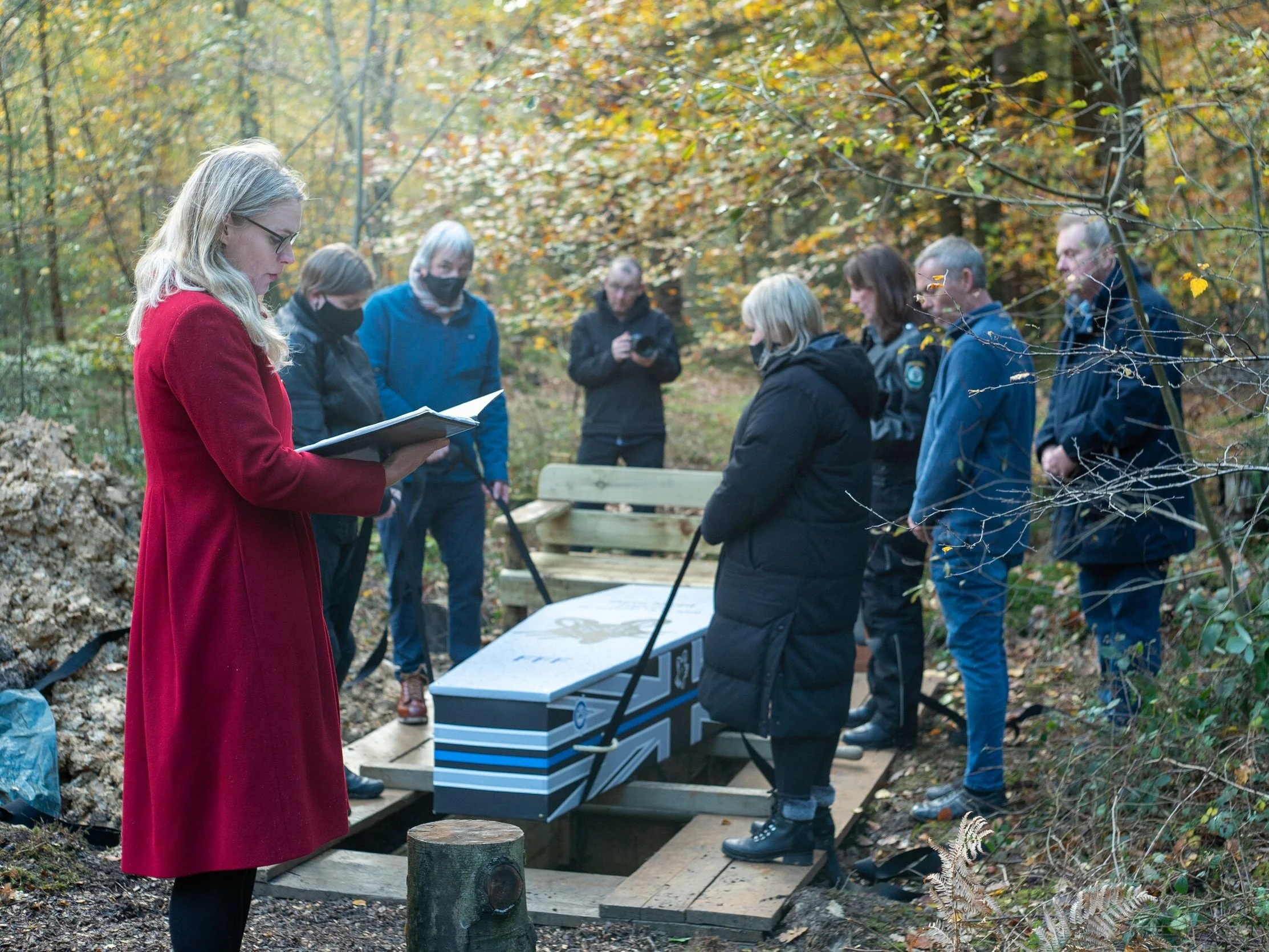 A woodland burial with mourners gathered around a coffin