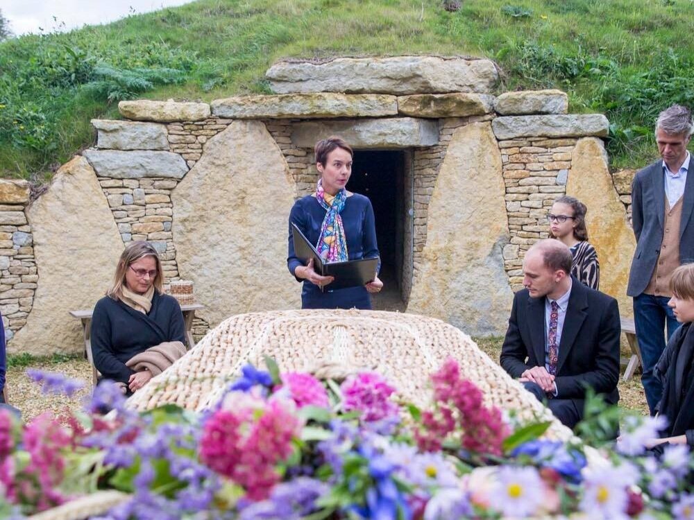 Rosalie Kuyvenhoven speaking at an outdoor funeral beside a woven coffin