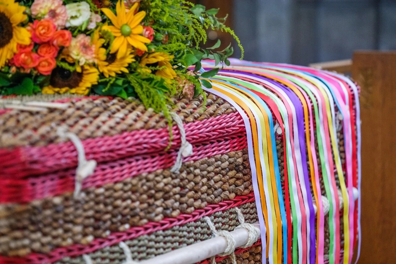 Colourful ribbons resting over Simon's woven coffin beside sunflowers and other flowers
