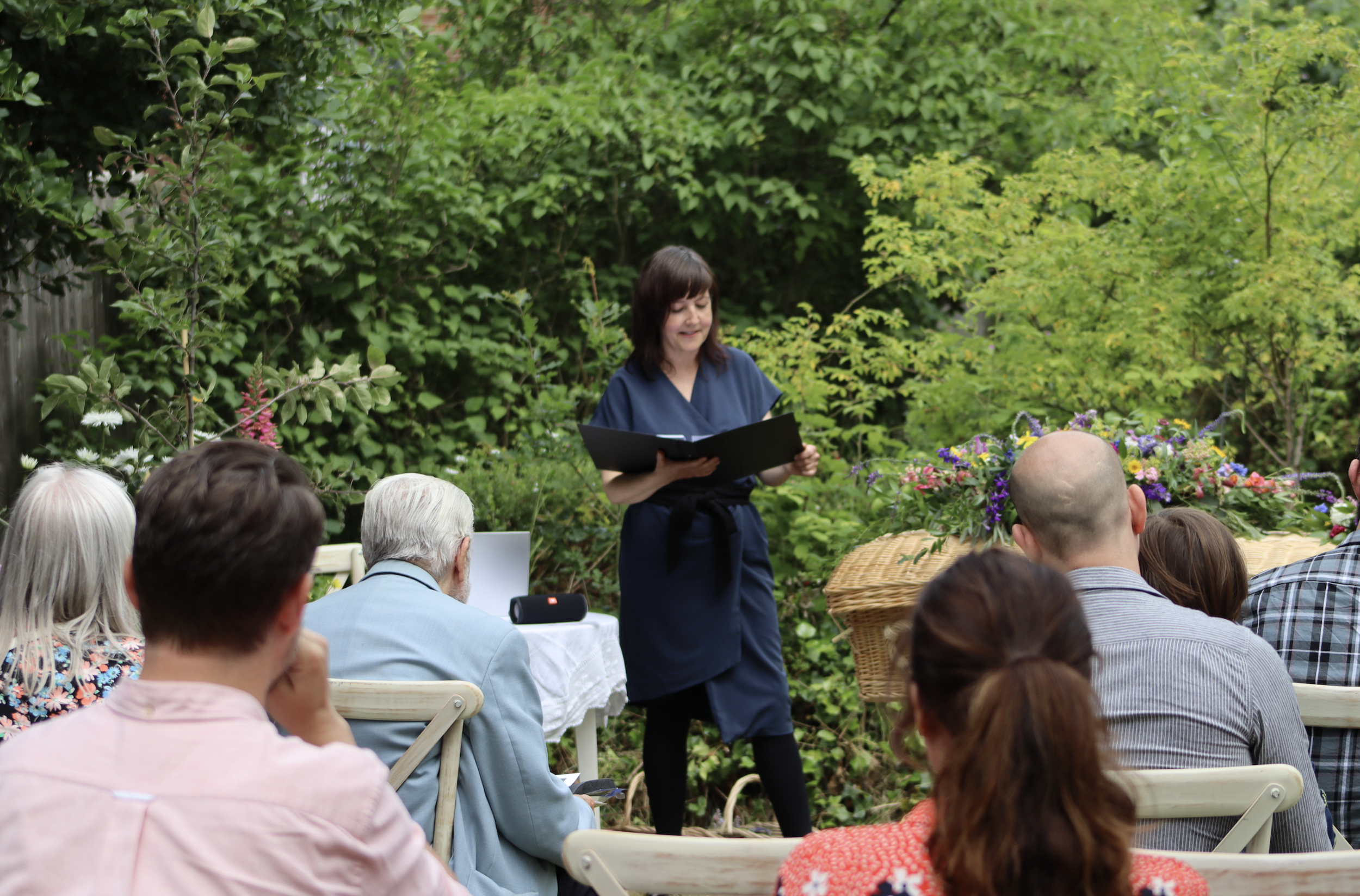 Sophie Duval leading an outdoor funeral ceremony beside a woven coffin decorated with flowers
