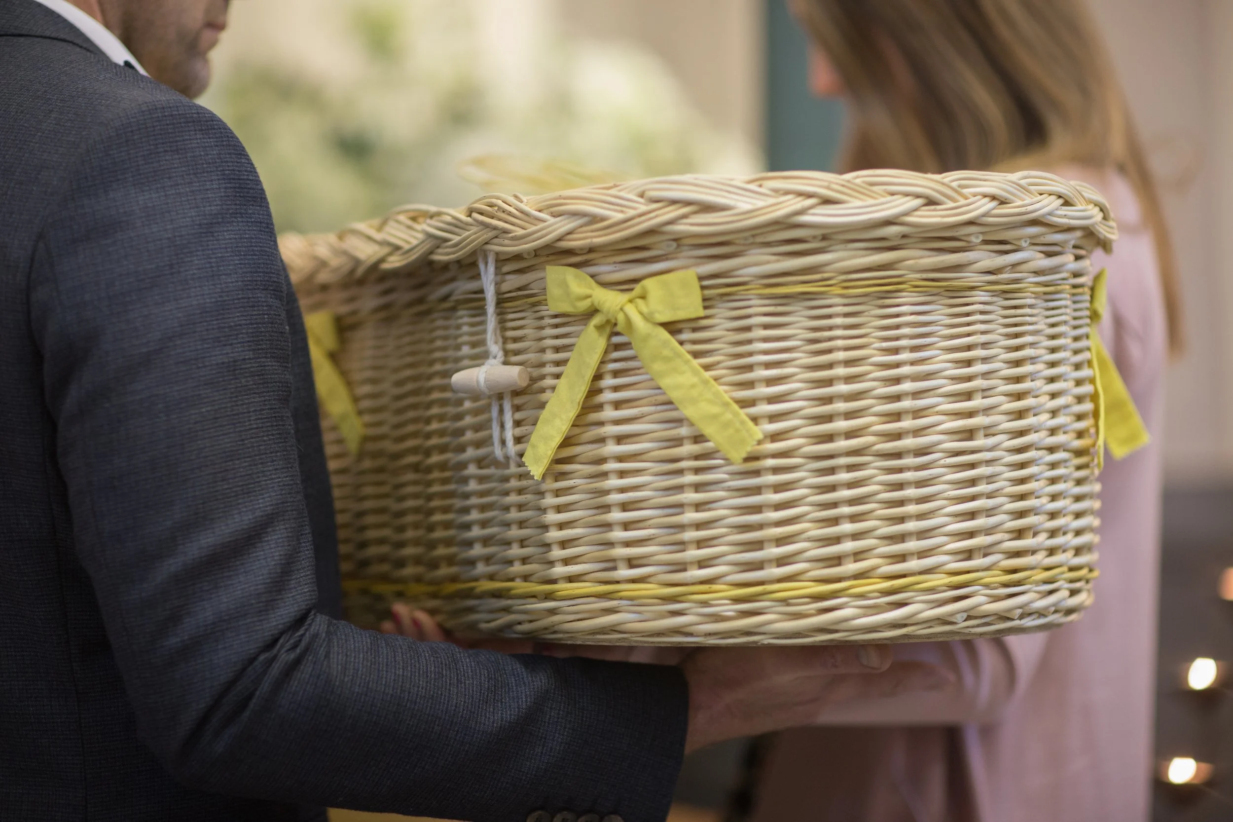 A small woven willow coffin with yellow ribbon, being carried by two people