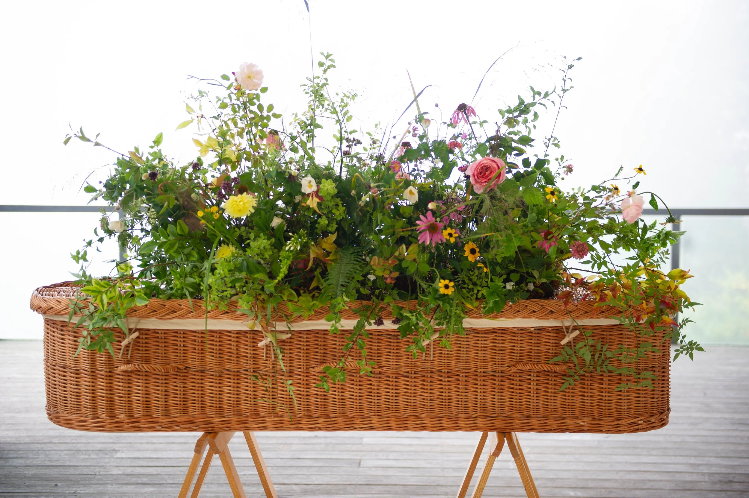 Bright garden flowers and greenery arranged across a woven coffin