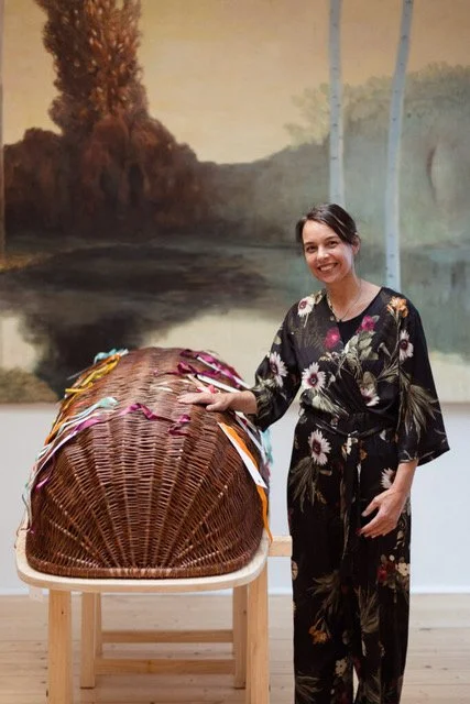 Rosalie standing beside a woven coffin decorated with colourful ribbons at a funeral