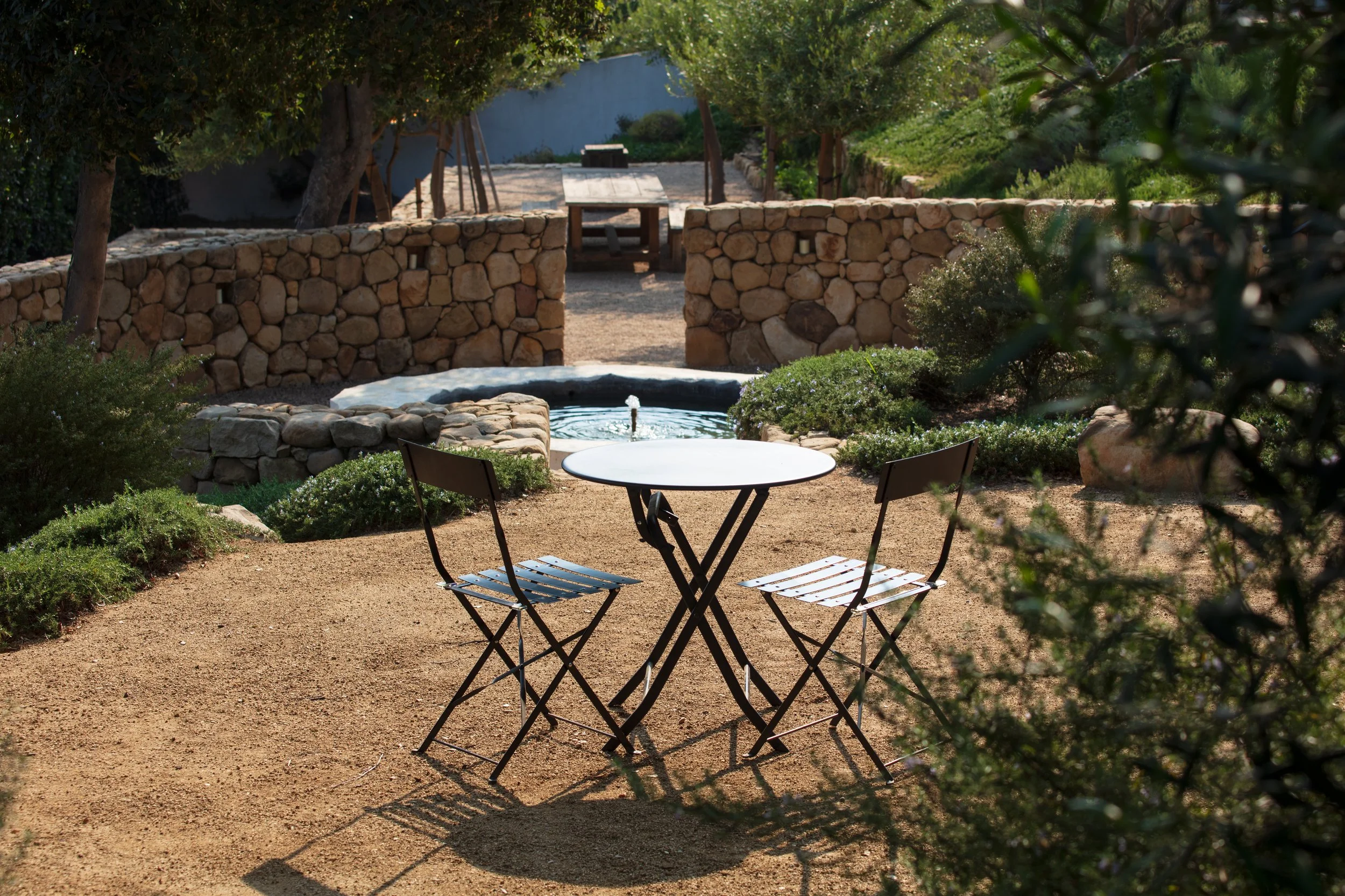  View from a hiking trail at a home in Santa Barbara, CA. The landscape design shows a cafe table with many patios and levels. A bocce ball court and vegetable garden are seen in the distance.  