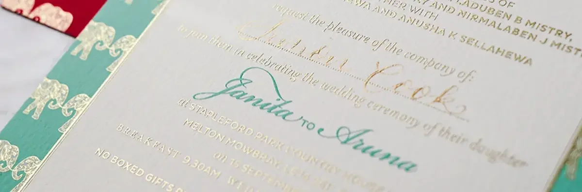 Close up of bespoke wedding invitation with teal border, gold foil elephant pattern and script font