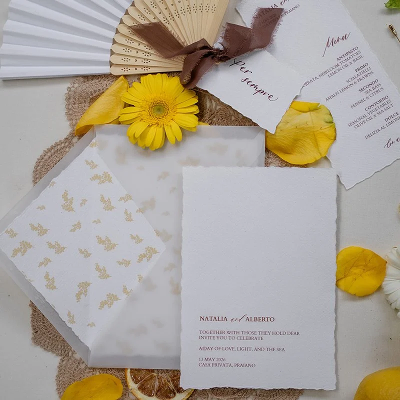 Ananya cards Amalfi Coast destination wedding stationery suite on torn edged paper beside a velum envelope with patterned liner, matching menu cards