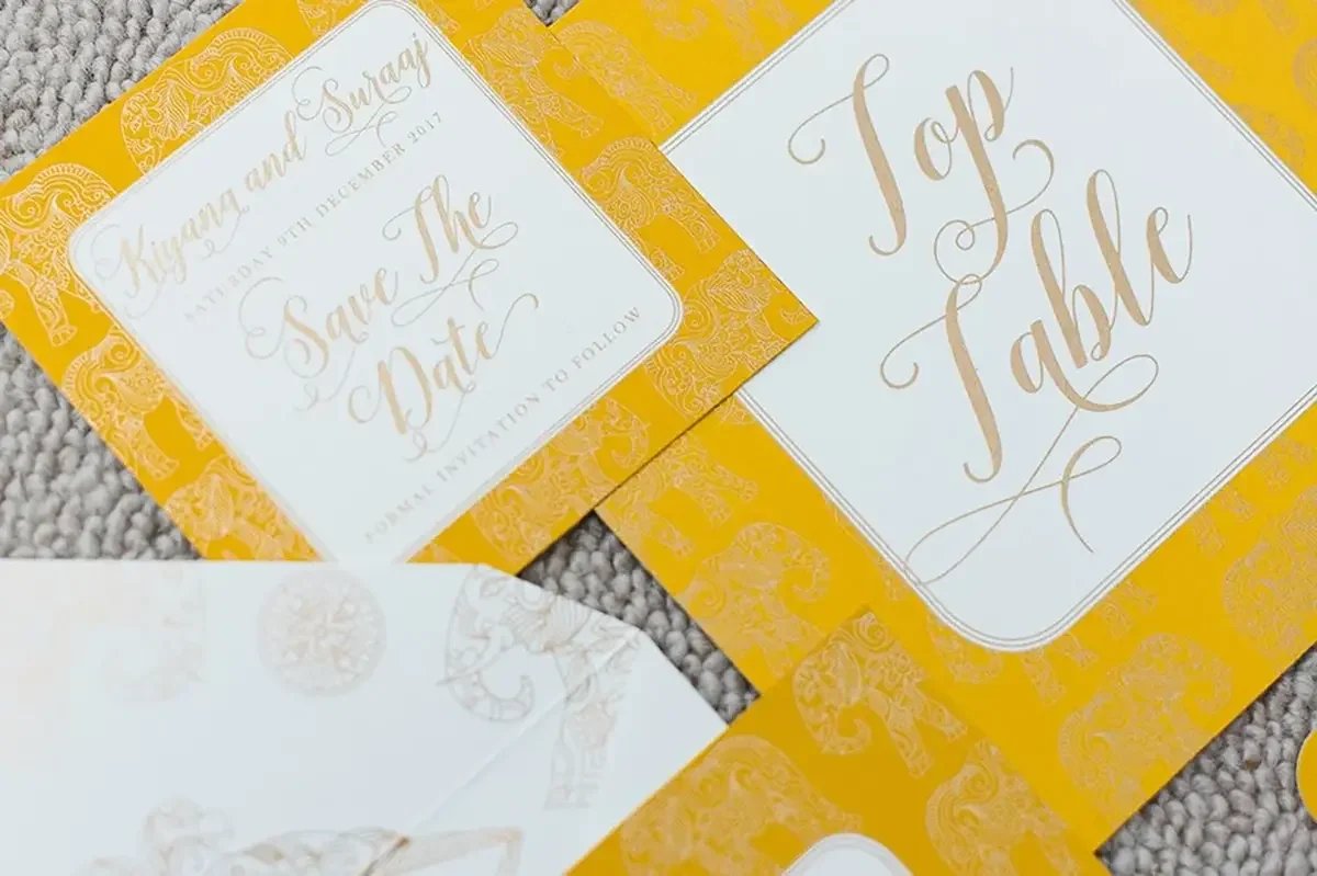 Flat lay of yellow wedding stationery with elephant pattern and gold script font