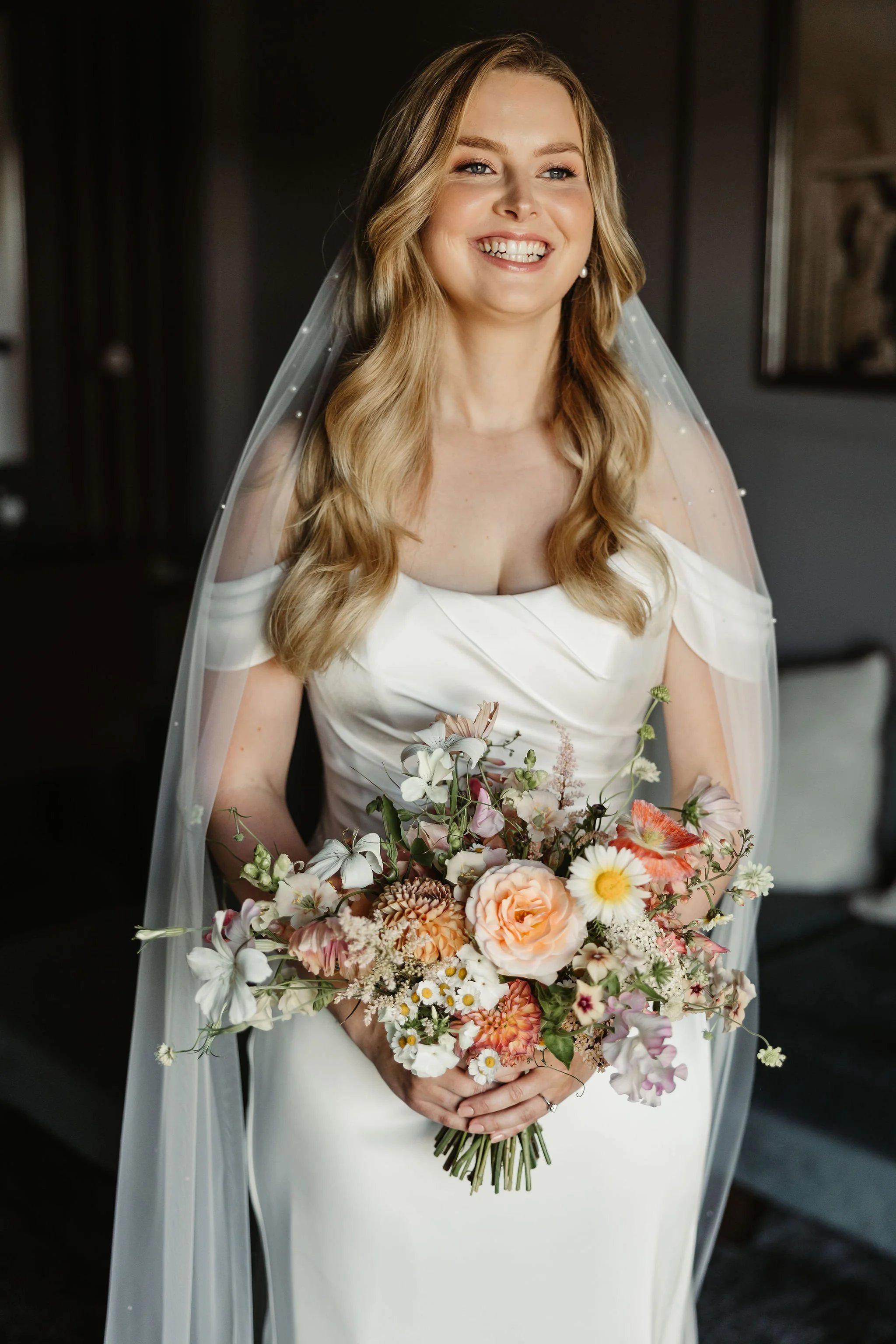 A smiling woman in a wedding dress holding a bouquet of flowers.
