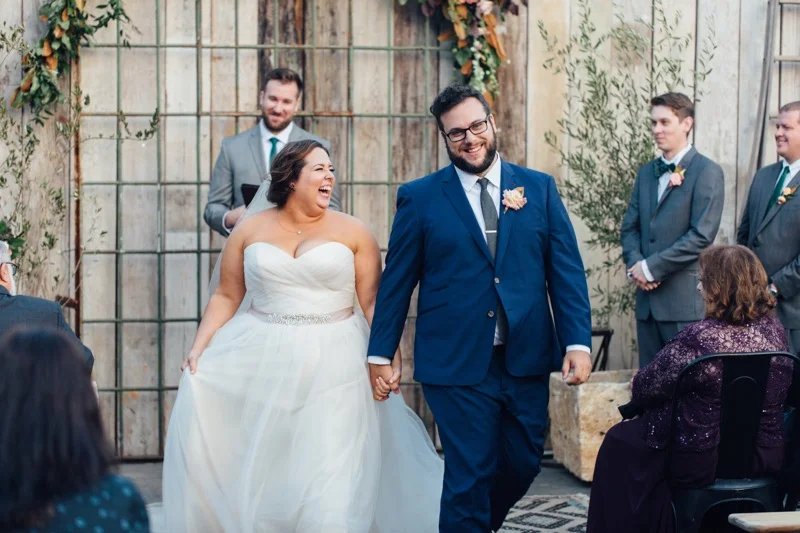 Just Married Bride & Groom Skipping Down The Aisle Wedding Photo. Eclectic Wedding at Big Daddy's Antiques Los Angeles, Groom in a blue suit, Della Curva Bride, Art & Soul Events
