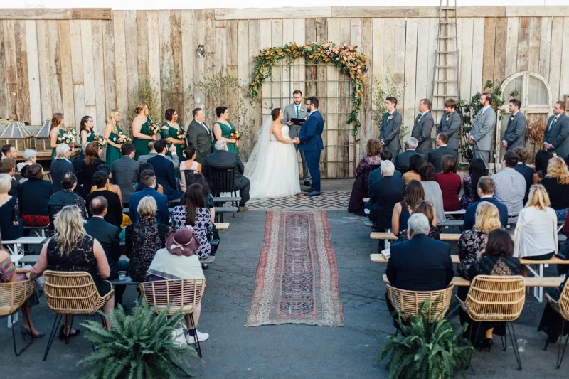 Outdoor Wedding Ceremony. Fall Green, peach, orange magnolia wedding arch. Fern & persian rug aisle runners. Eclectic Wedding at Big Daddy's Antiques Los Angeles, Planning & Design Art & Soul Events