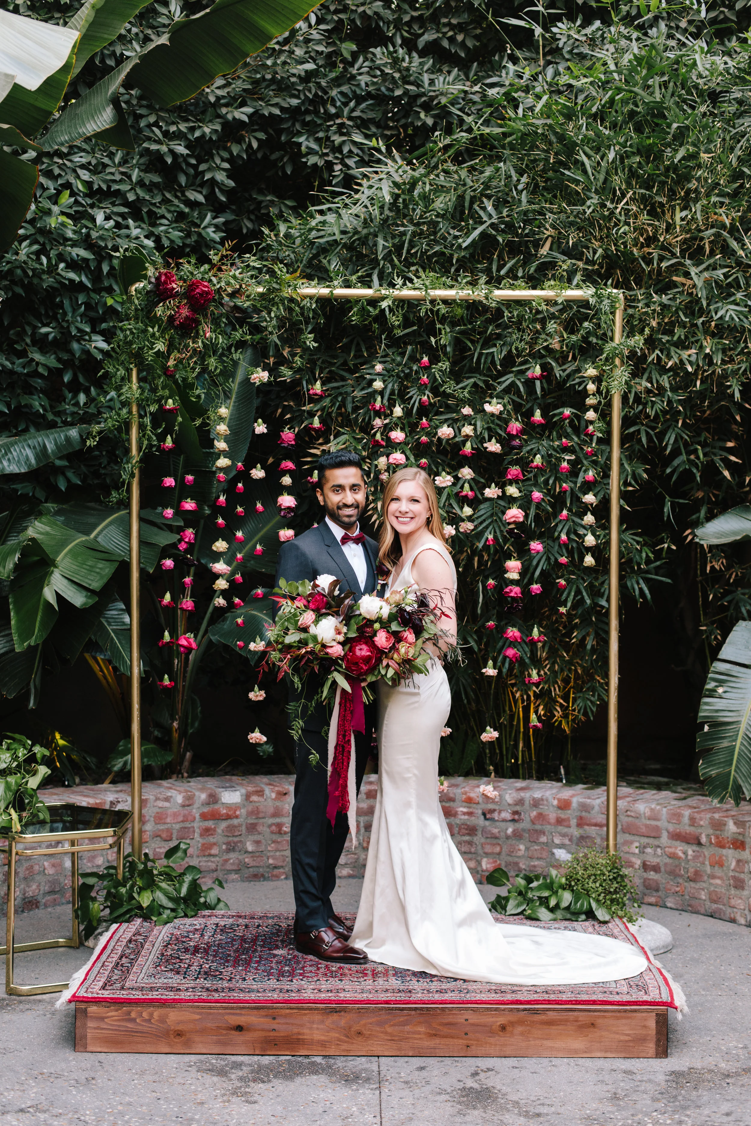 Bride holding a wild burgundy, crimson, merlot and white bridal bouquet with peonies and garden roses. Sri Lankan Groom in a charcoal Dolce Gabbana Suit & Boutonniere, Millwick Wedding in DTLA