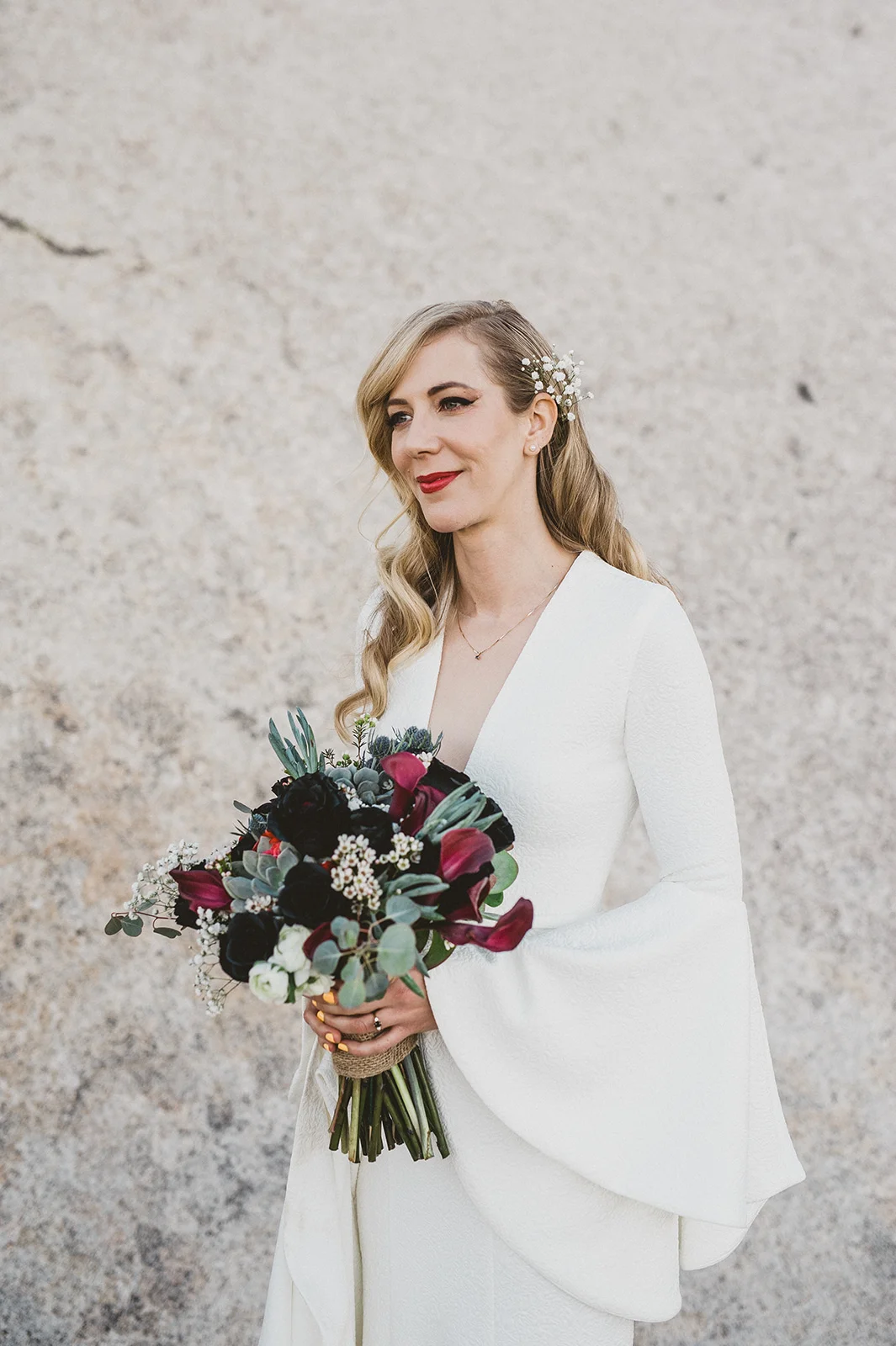 Beautiful blonde bride with old hollywood glam 1930's waves, Suzanne Harward The Bell Sleeve Wedding Dress, Indian Cove Amphitheatre, Joshua Tree Wedding Ceremony holding a black rose bouquet