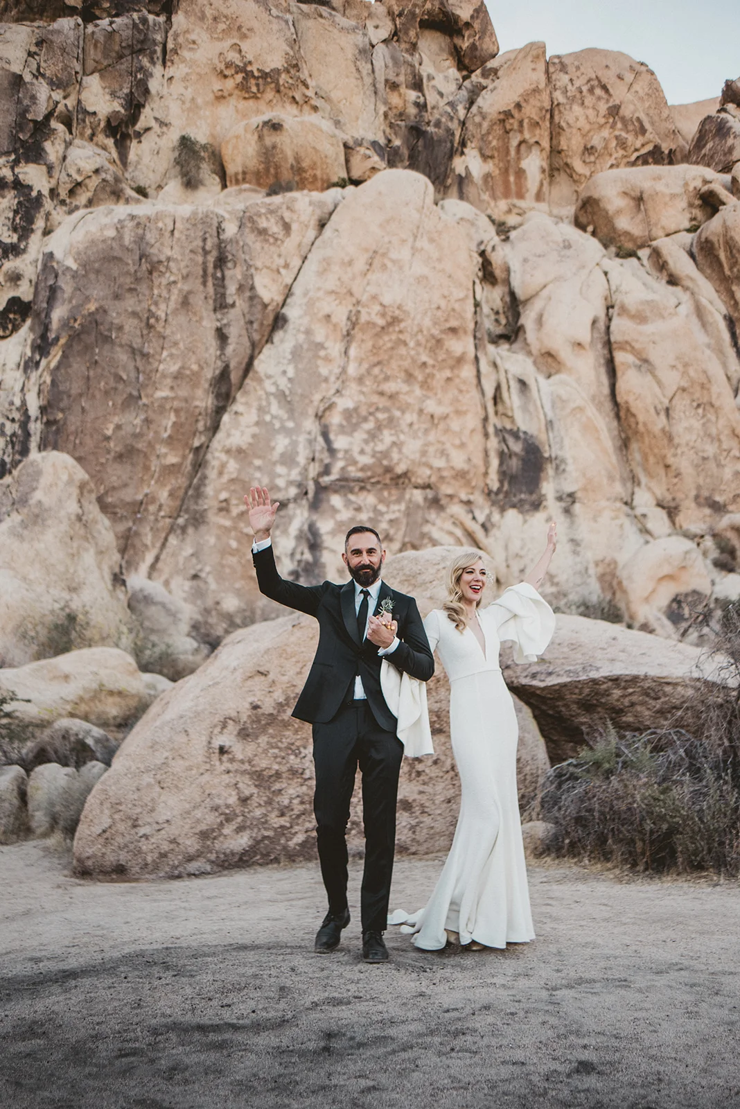 Wedding portraits. Beautiful blonde bride in a Suzanne Harward The Bell Sleeve Wedding Dress at the Indian Cove Amphitheatre in Joshua Tree Ceremony, Hot bearded Groom in a black suit