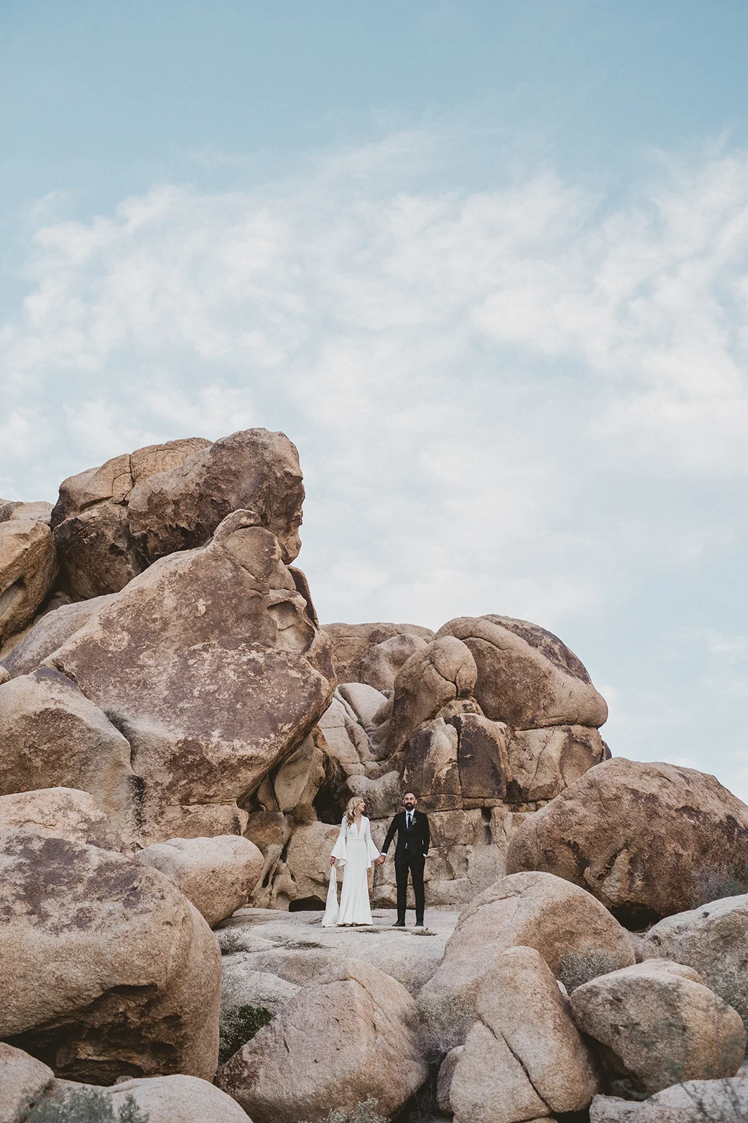 Epic Wedding portraits. Beautiful blonde bride in a Suzanne Harward The Bell Sleeve Wedding Dress at the Indian Cove Amphitheatre in Joshua Tree Ceremony, Hot bearded Groom in a black suit
