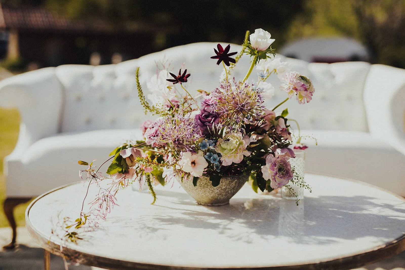 White Found Rentals sofa with a marble cocktail table with a wild asymmetrical lavender, white, and blue, spring flower arrangement. Planned by Art & Soul Events