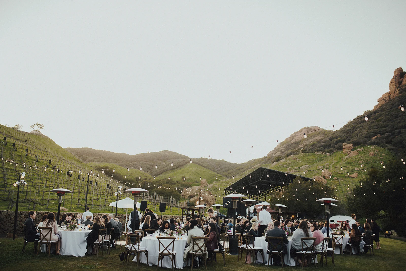 Outdoor Malibu vineyard wedding with string lights, crossback vineyard chairs, round wedding tables with white linens. Saddlerock Ranch, Camp Cabernet venue. Art & Soul Events