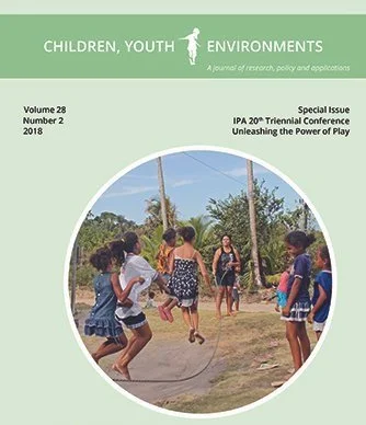 Children playing jump rope outdoors in a grassy area surrounded by trees.