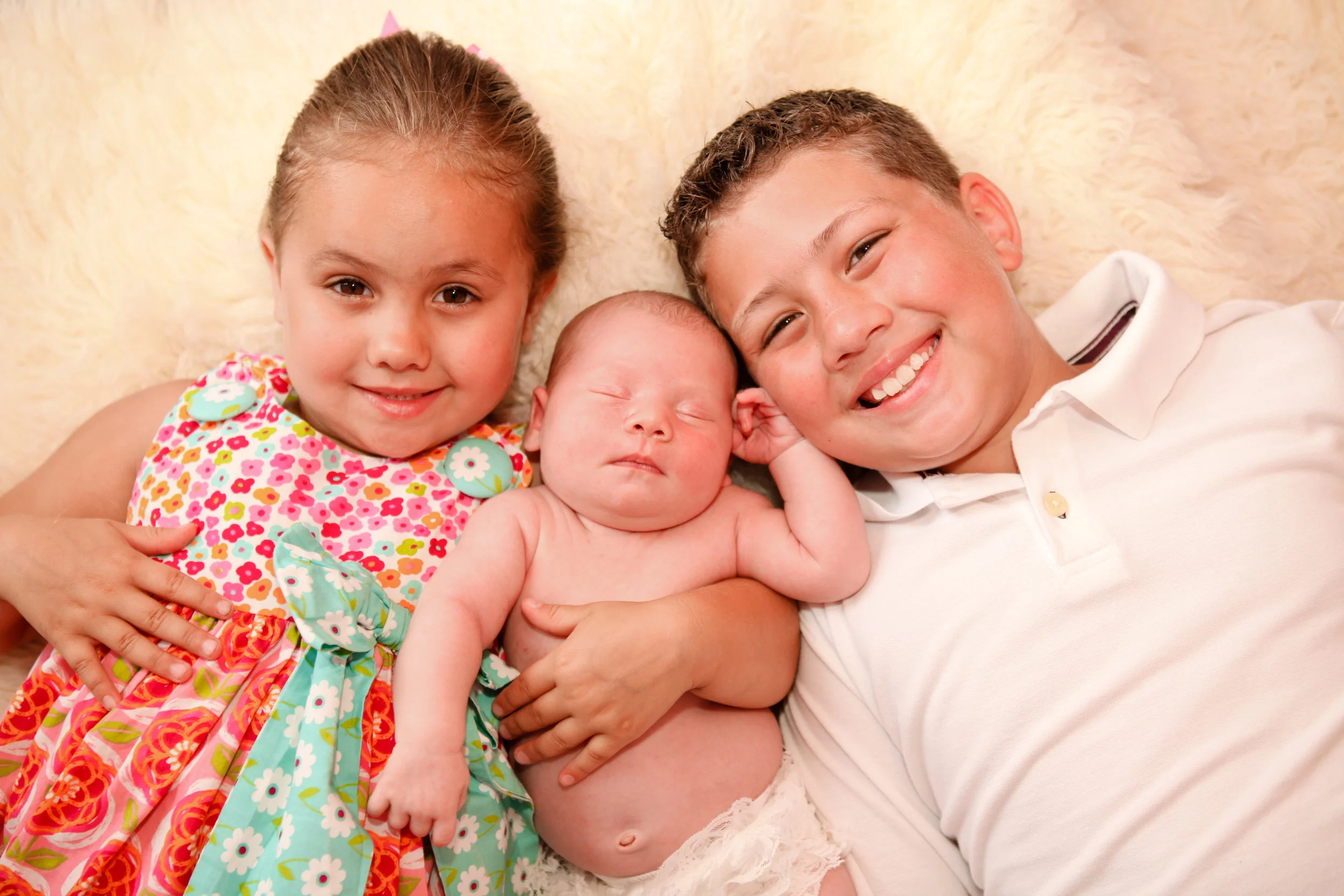 a little girl and little boy smiling holding their newborn sibling