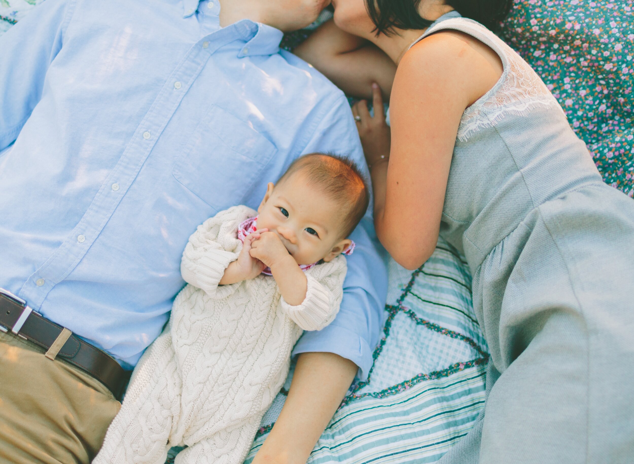 a-family-of-three-lying-on-a-blanket-outside-6G9PR78.jpg