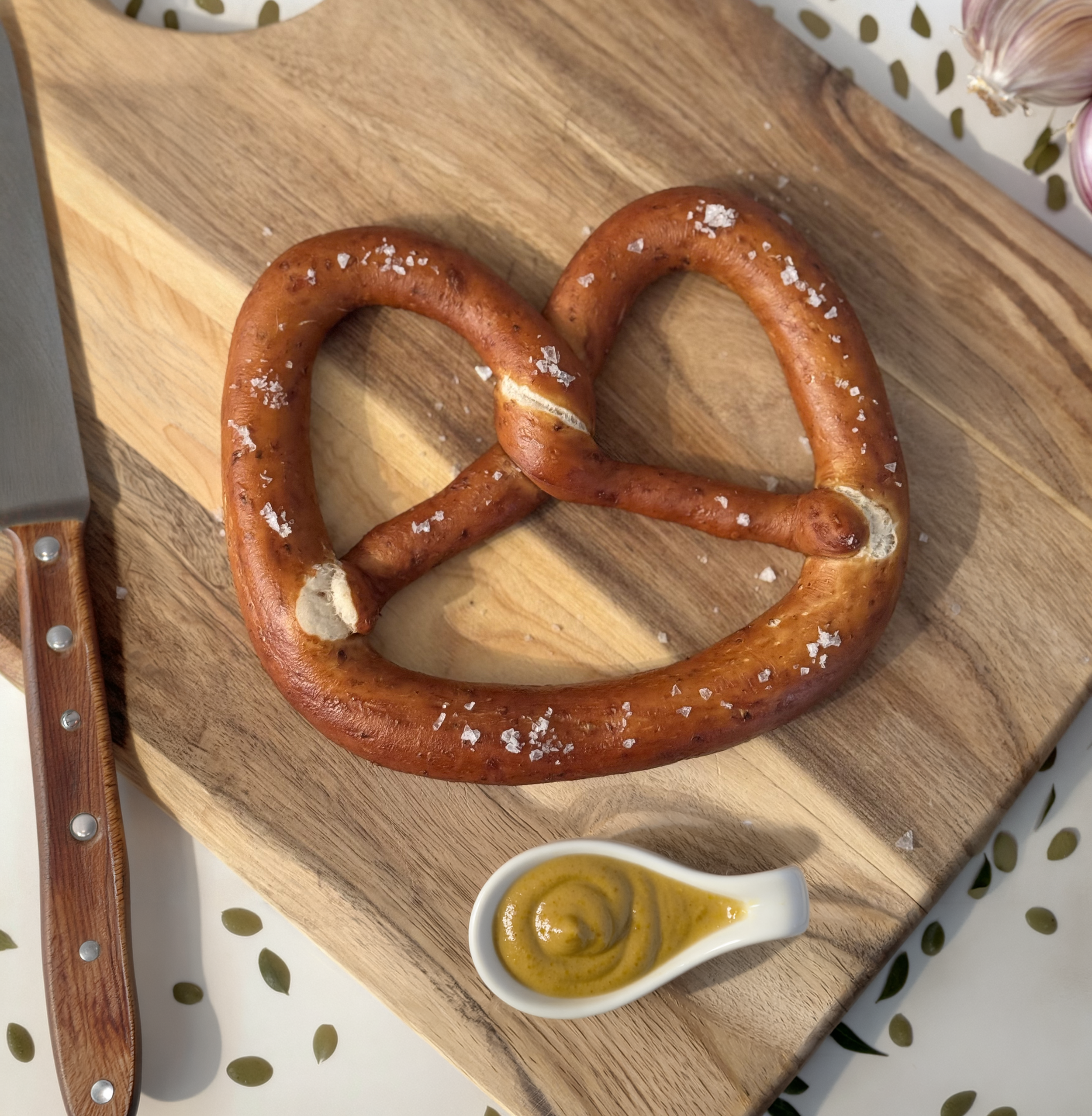 The Bread Shed Spent Grain Standard Pretzel on a cutting board with mustard dipping sauce.