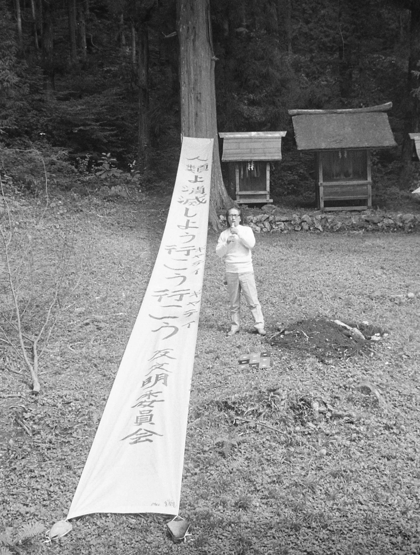 Japanese artist Yutaka Matsuzawa and his “Banner of Vanishing (Humans, Let’s Vanish, Let’s Go, Let’s Go, Gate, Gate, Anti-Civilization Committee)” (1966), at Mount Misa, Japan, 1970 (photo © Hanaga Mitsutoshi) (click to enlarge)