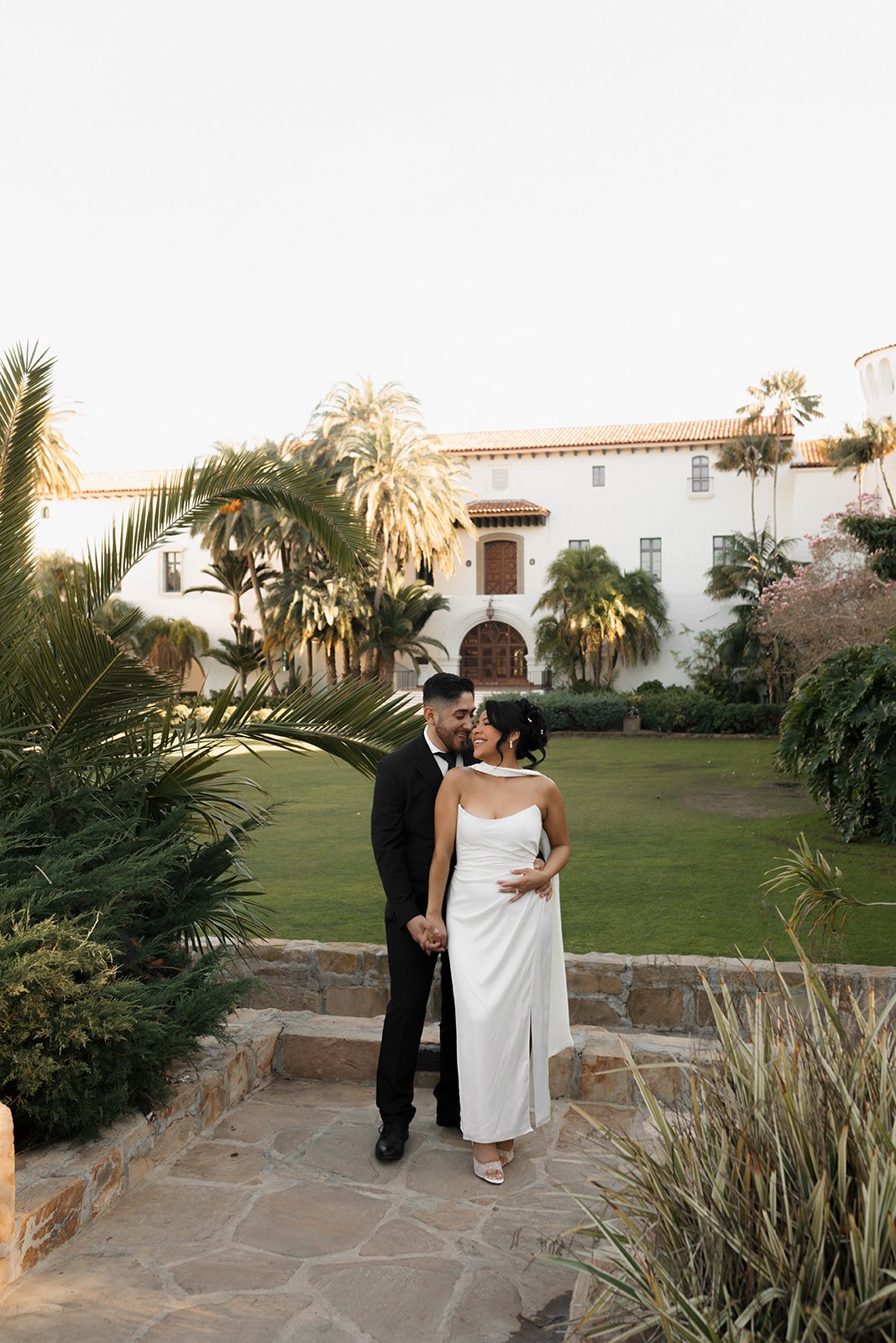 Romantic candid of groom hugging bride from behind during elopement at the Santa Barbara Courthouse Sunken Gardens, his face nestled between her face and neck in an intimate moment