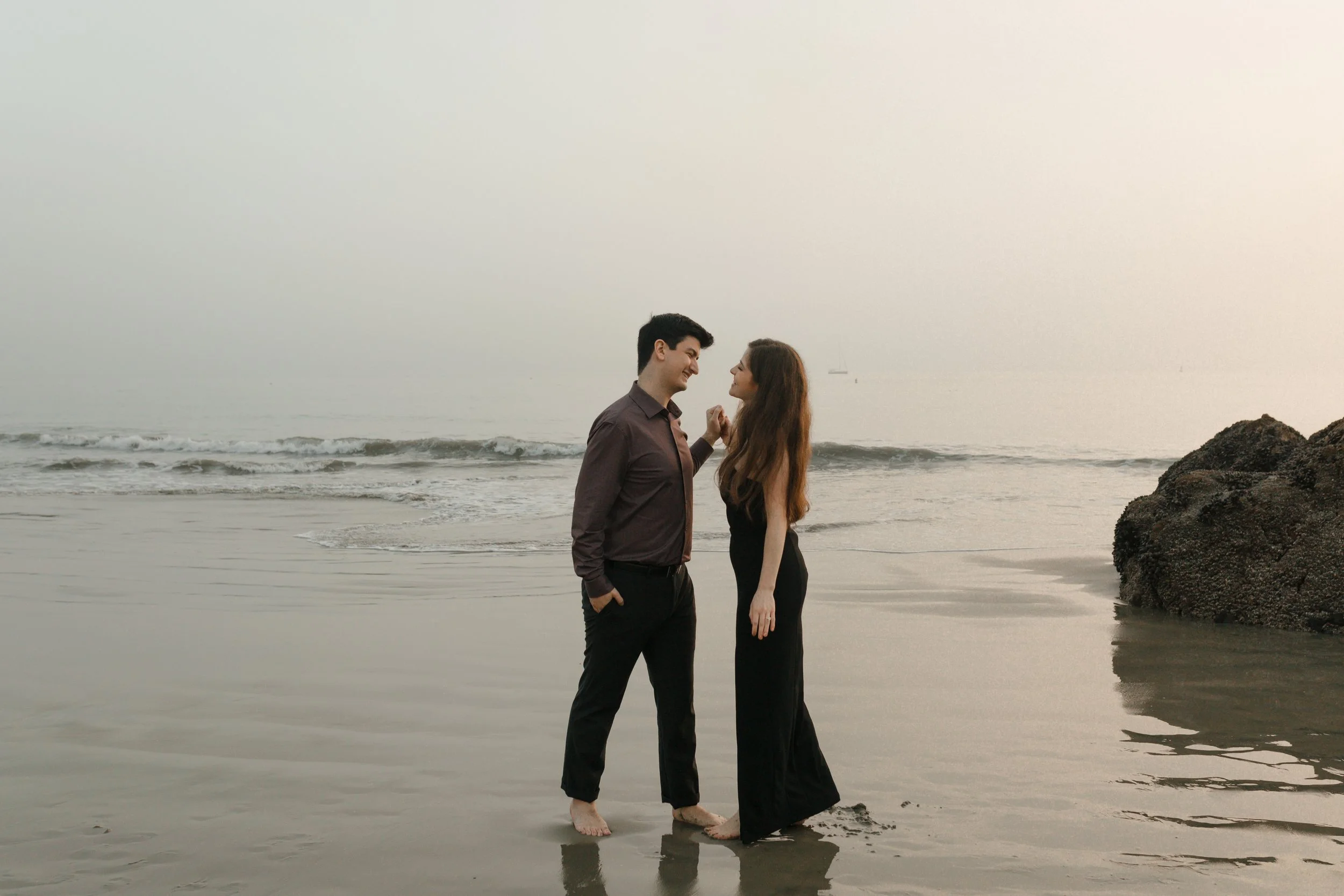couple looking at eachother romantic holding hands leaning in on the beach from proposal in newport beach