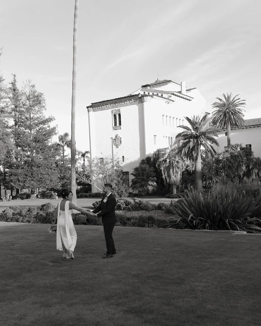 Black and white candid of couple holding hands and looking at each other while running through the gardens at the Santa Barbara Courthouse Sunken Gardens in a joyful elopement moment