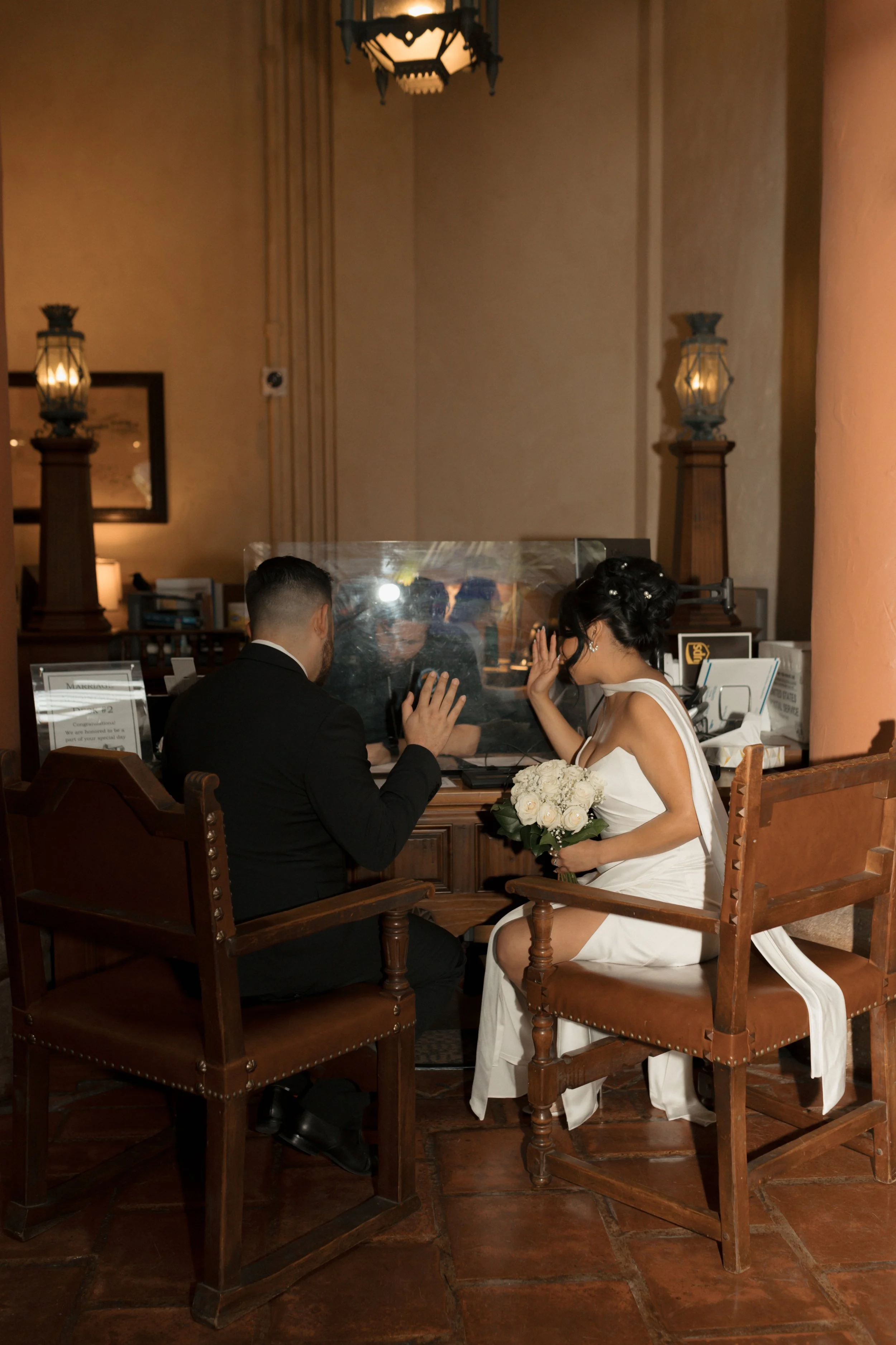 Couple holding up their hands while signing marriage documents inside the Hall of Records at the Santa Barbara Courthouse during their elopement ceremony