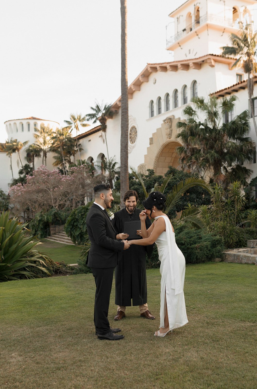 Bride wiping away a tear while holding hands with groom during elopement ceremony at the Santa Barbara Courthouse Sunken Gardens