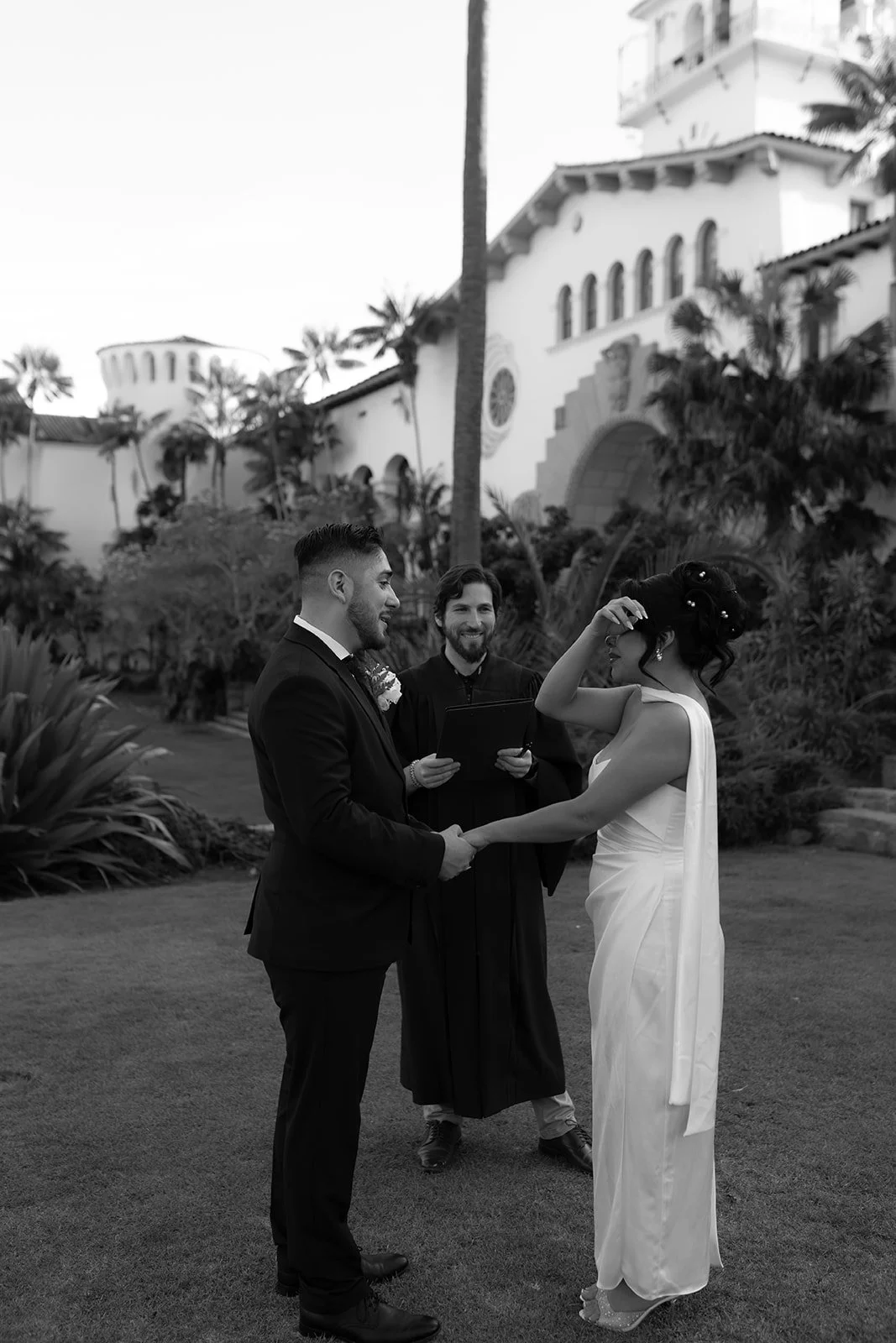 Black and white photo of bride crying while holding hands during elopement ceremony at the Santa Barbara Courthouse Sunken Gardens