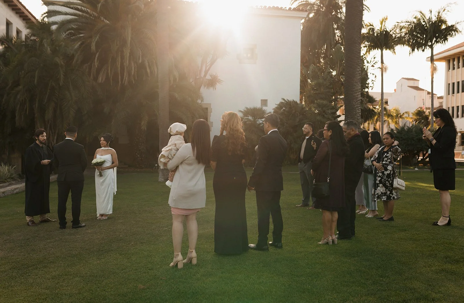 Golden hour ceremony photo from a distance, POV of guests watching couple’s elopement ceremony at the Santa Barbara Courthouse Sunken Gardens with warm light over the scene