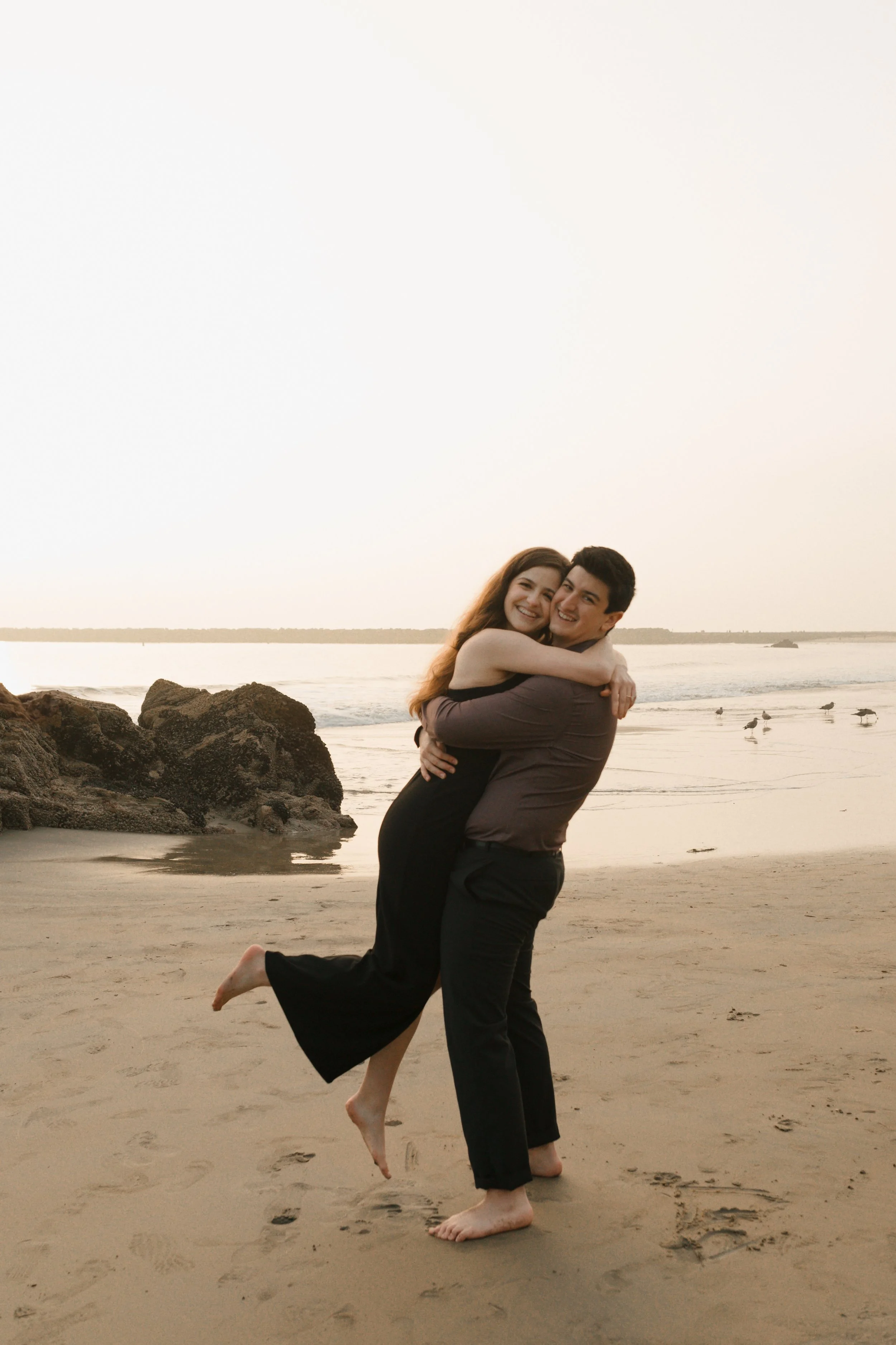 couple on the beach hugging and lifting up from proposal in newport beach