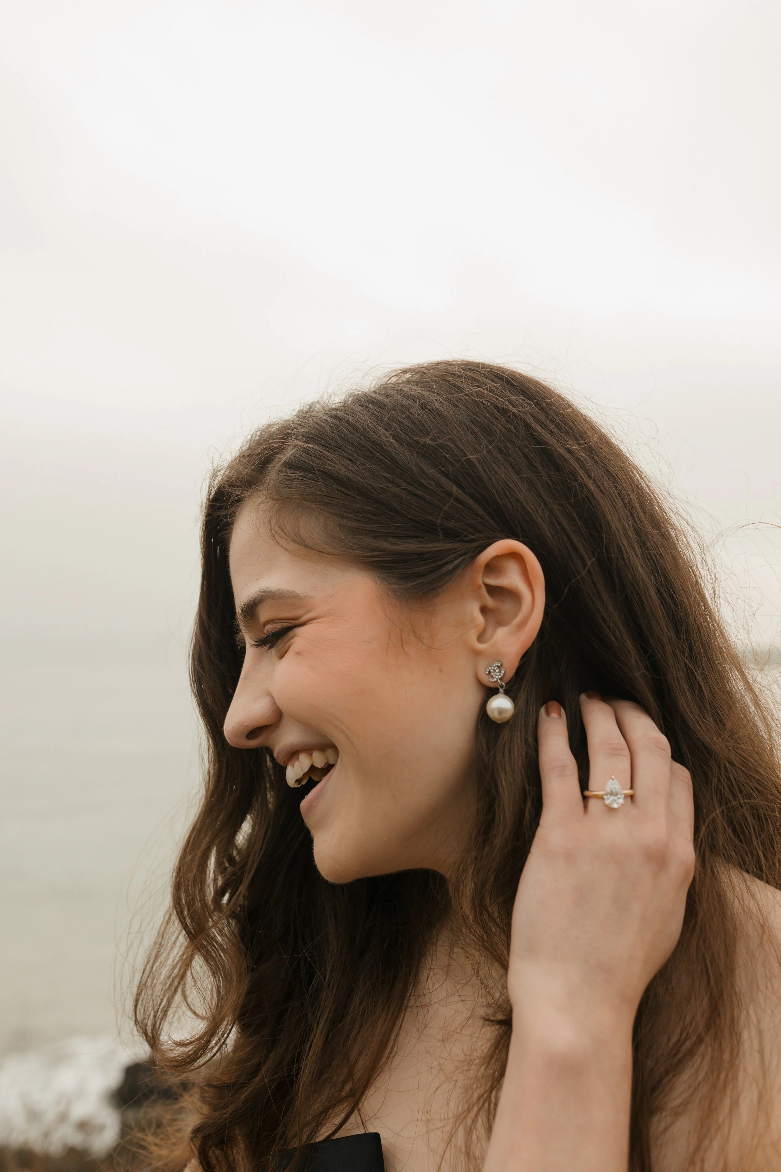 close up photo of girl pulling her hair back with ring fingers showing off the ring from the proposal at lookout in newport beach with the ocean in background