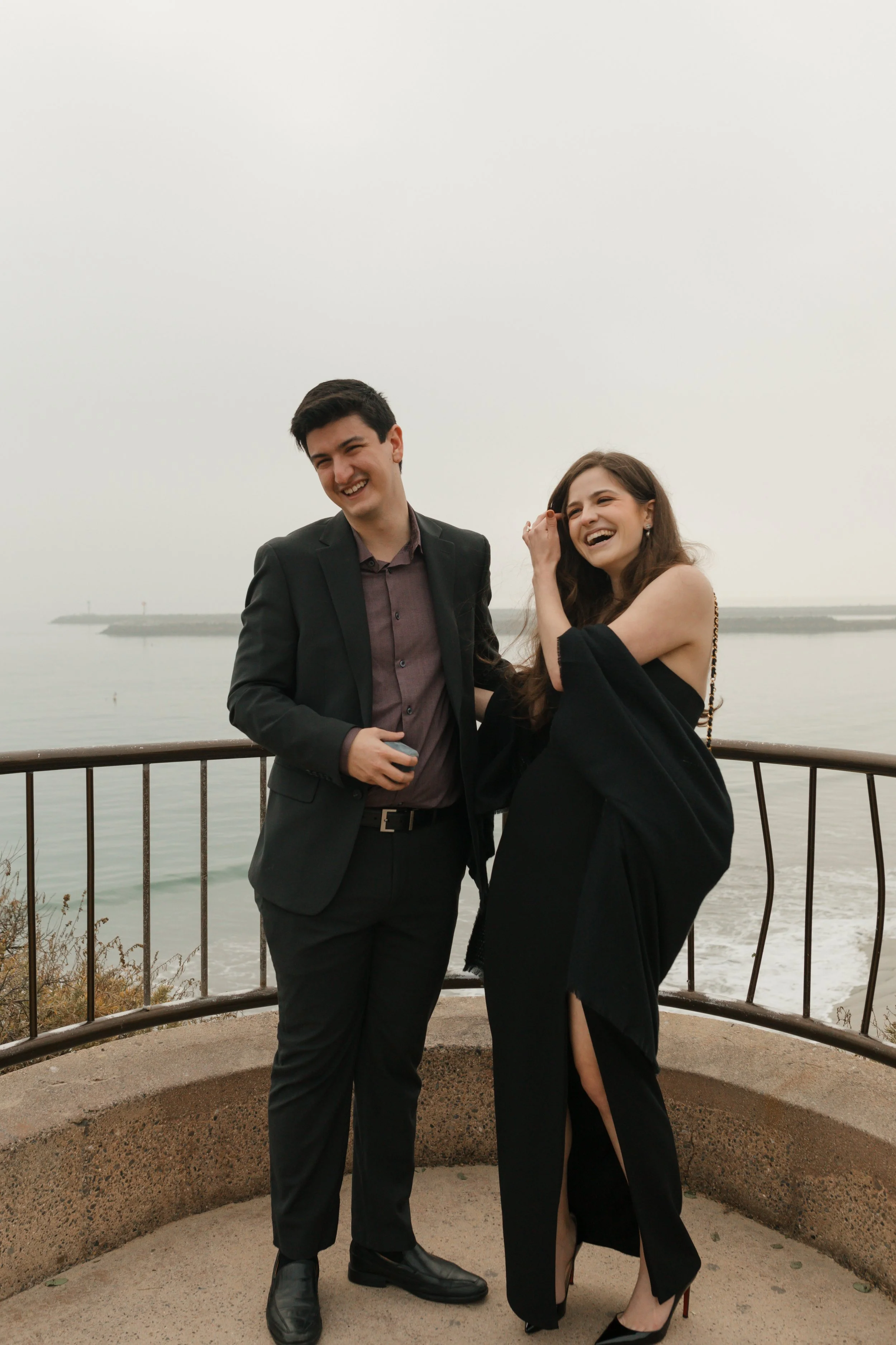 candid laughing photo of couple from proposal at lookout in newport beach with the ocean in background