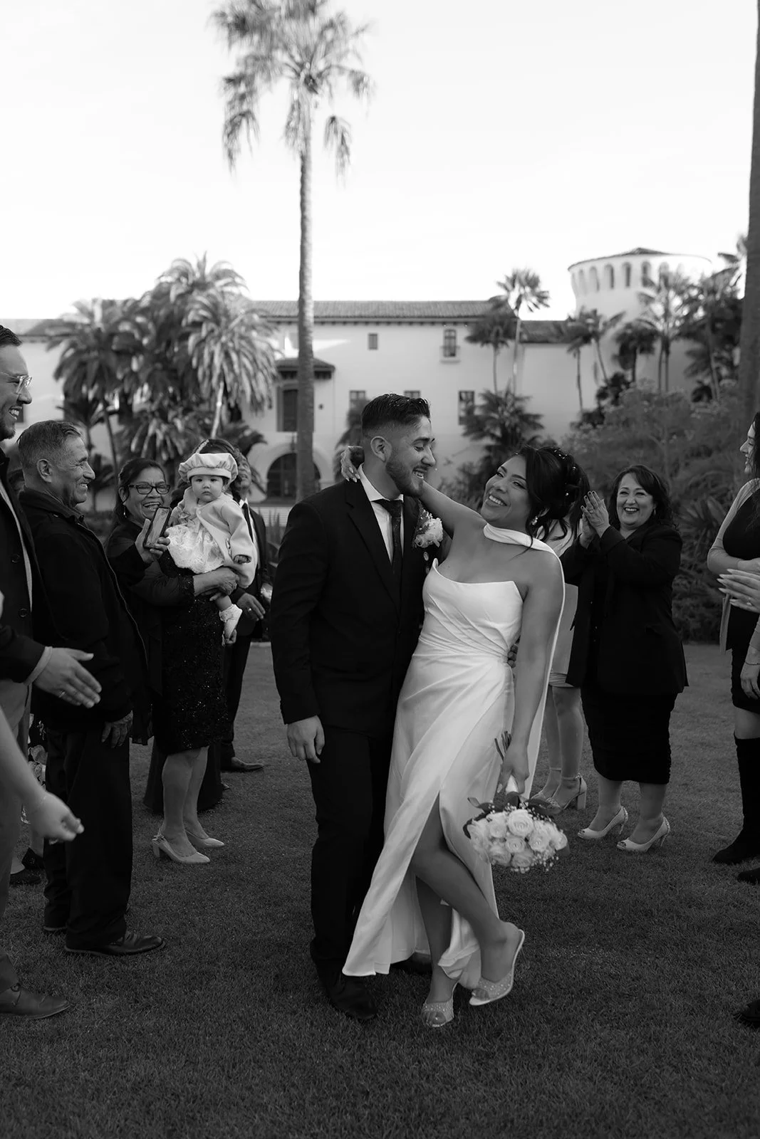 Black and white candid of bride holding onto groom with her arms around his neck during a dip kiss, smiling in celebration after ceremony at the Santa Barbara Courthouse Sunken Gardens